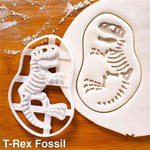 May include: A white plastic T-Rex fossil cookie cutter next to a cookie with a T-Rex fossil imprint. The cutter has a frame around the dinosaur skeleton design. The text "T-Rex Fossil" is at the bottom of the image.