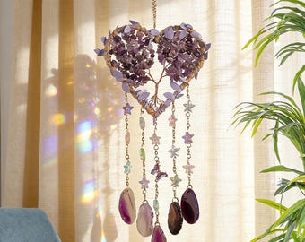 May include: A heart-shaped amethyst crystal suncatcher with a tree of life design. The suncatcher features purple gemstones, star-shaped beads, and hanging agate slices. It hangs from a gold chain, creating a decorative and spiritual accent.