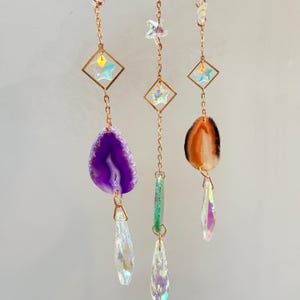 Pu&ograve; includere: Tre ornamenti decorativi sospesi. Ogni ornamento presenta una catena color rame con una cornice a forma di diamante e un pendente di cristallo. Uno ha una fetta di agata viola, un altro un cristallo verde e il terzo una fetta di agata arancione.