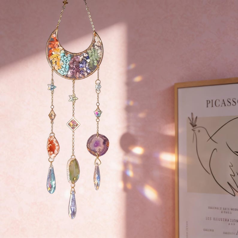 Pu&ograve; includere: Un acchiappasole a tema celeste con una luna a mezzaluna piena di pietre colorate. Catene dorate sospendono cristalli a forma di stella e gemma, creando un pezzo decorativo e accattivante. L'acchiappasole &egrave; progettato per catturare e riflettere la luce.