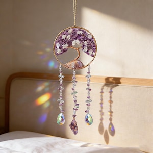 Può includere: Un acchiappasole decorativo con un design ad albero della vita. La cornice circolare è riempita di pietre preziose viola e bianche, con un tronco d'albero color rame. Sotto pendono tre fili di perline e pendenti di cristallo, con una catena dorata per appendere.