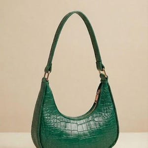 May include: A green, crescent-shaped handbag with a crocodile-skin texture. The bag has a matching handle and a gold-colored zipper. The bag is made of a shiny material and is a solid, vibrant green color.