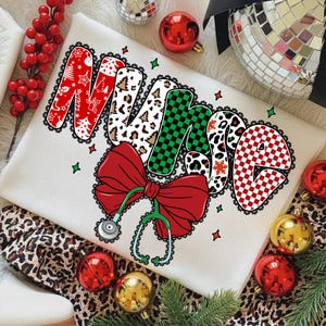 Peut inclure: Un sweat-shirt blanc avec le mot "NURSE" dans un design festif. Les lettres pr&eacute;sentent des motifs tels que des arbres de No&euml;l, des imprim&eacute;s l&eacute;opard et des motifs &agrave; carreaux. Un n&oelig;ud rouge et un st&eacute;thoscope sont &eacute;galement pr&eacute;sents. Des boules de No&euml;l entourent le sweat-shirt.