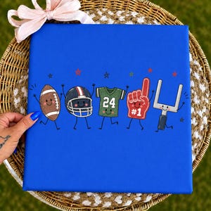 May include: A bright blue square canvas featuring a cartoon illustration of five football-themed characters with smiling faces and thin black limbs. The characters include a brown football, a black helmet, a green jersey with the number 24, a red foam finger with the text #1, and a white goalpost, all accented by small red and blue stars.