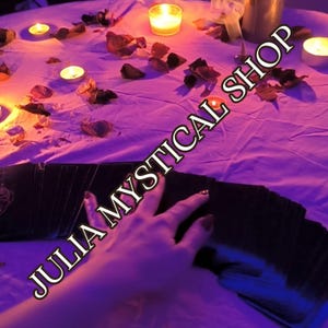 May include: A deck of black tarot cards spread out on a white cloth surface illuminated by purple lighting and several small lit candles. Scattered dried flower petals surround the cards, and the text JULIA MYSTICAL SHOP is overlaid in white.