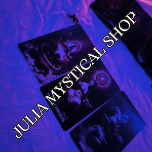 May include: Three rectangular tarot cards with dark, moody illustrations are arranged on a surface. The cards feature the text Queen of Cups, Ace of Pentacles, and Knight of Swords. The text JULIA MYSTICAL SHOP is overlaid diagonally across the image.