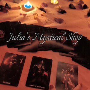 May include: A collection of tarot cards with the text "Julia's Mystical Shop" and three cards visible, including "The Devil" and "Knight of Pentacles." The scene is illuminated by candlelight and scattered petals.