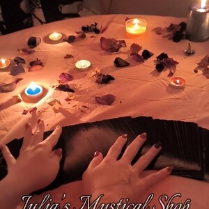 May include: A dimly lit scene with lit candles, dried flower petals, and a deck of cards. The text "Julia's Mystical Shop" is visible. The overall theme suggests a mystical or spiritual setting.