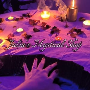 May include: A white tablecloth covered in scattered dried flower petals, multiple lit candles, and a thin trail of incense smoke. A deck of black tarot cards is fanned out in the foreground with the text Julia's Mystical Shop overlaid in white.