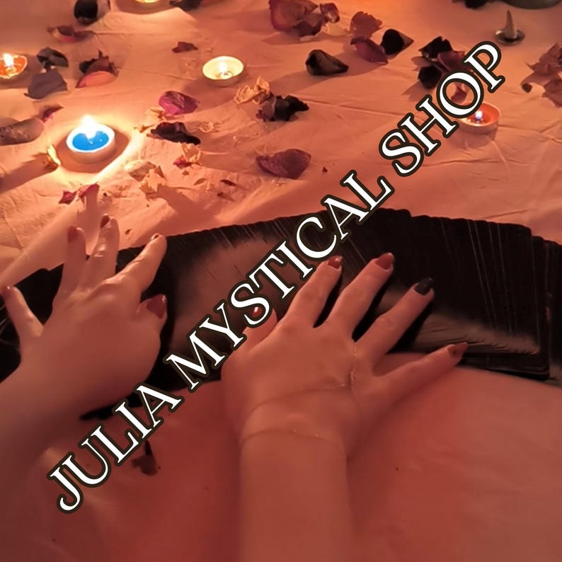 May include: A deck of black tarot cards spread out on a light-colored surface scattered with dried flower petals and illuminated by several small lit candles. The text JULIA MYSTICAL SHOP is overlaid across the center of the image.