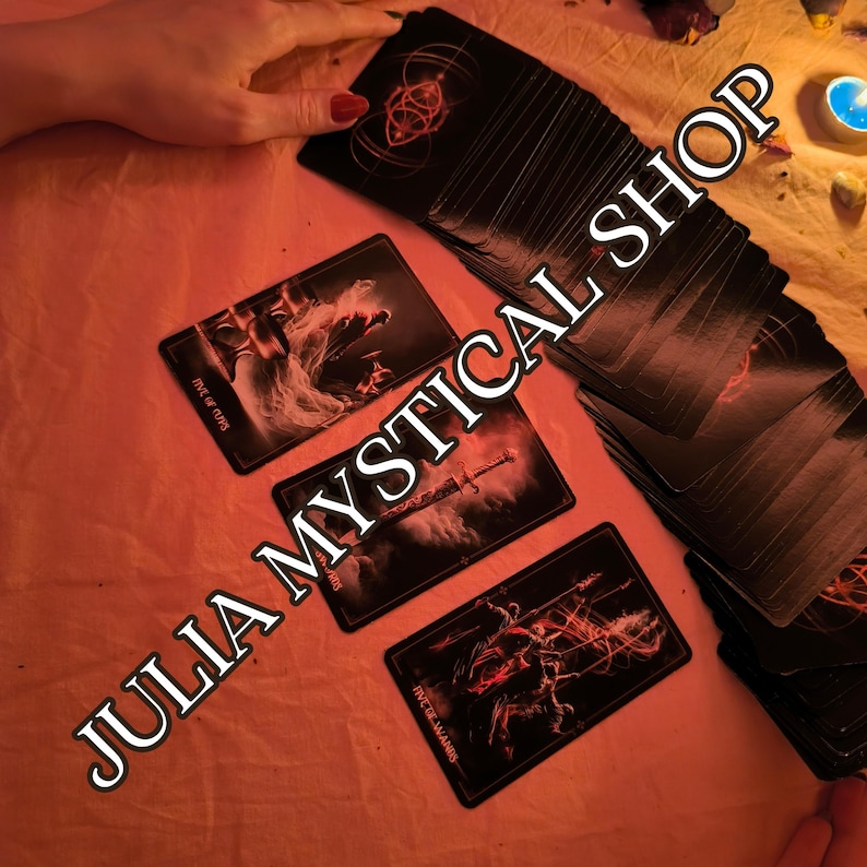 May include: A deck of black tarot cards with red accents, featuring the Five of Cups, Ace of Swords, and Five of Wands cards laid out. The cards display intricate illustrations and the text JULIA MYSTICAL SHOP is overlaid across the image.