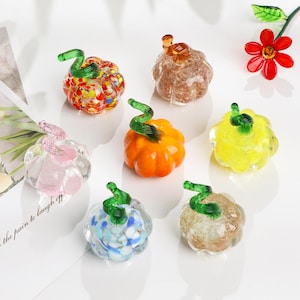 Peut inclure: Plusieurs petites citrouilles décoratives en verre de différentes couleurs, dont orange, jaune, rose et marron. Chaque citrouille a une tige verte en spirale. Certaines ont des motifs tachetés.