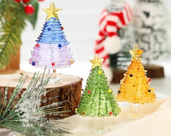 May include: Three decorative glass Christmas trees in blue, green, and yellow, each topped with a gold star. The trees have a textured, layered design and are set on clear glass bases. The trees are decorated with small, colorful beads.