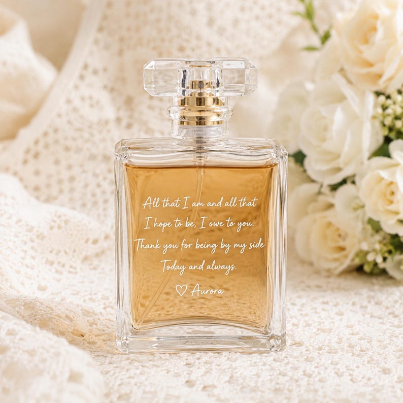 May include: A rectangular clear glass perfume bottle filled with amber liquid. The front features white engraved text: All that I am and all that I hope to be, I owe to you. Thank you for being by my side. Today and always. ♡ Aurora. It has a clear cap.