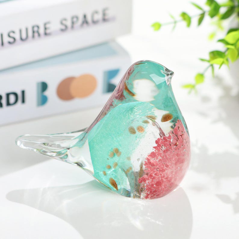 May include: A decorative glass bird figurine with a clear, turquoise, and red design. The bird has a transparent tail and wings, with gold flecks throughout the body. The figurine is a decorative item.