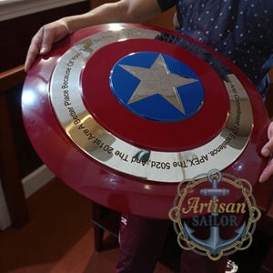 Captain America shield replica, metal wall decor with red/white/blue and star; engraved outer ring, personalized cosplay gift.