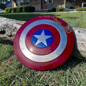 May include: A circular shield featuring a concentric design with a deep red outer ring, a metallic silver middle ring, and a vibrant blue center circle containing a large, five-pointed silver star. The surface has a smooth, reflective finish.