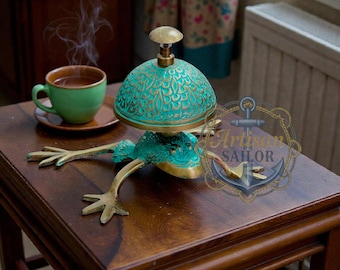 May include: A brass frog-shaped incense burner with a turquoise patina and gold accents. A green teacup and saucer sit on a wooden table. Steam rises from the cup, suggesting a warm beverage.