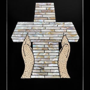 May include: A decorative cross mosaic with a mother-of-pearl design, held by two hands with a cracked, textured appearance. The cross is made of rectangular pieces, set against a black background.