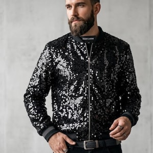 Può includere: Giacca bomber nera con paillettes, cerniera argentata e colletto e polsini a coste. La giacca ha una base nera con paillettes argentate. Un capo di abbigliamento esterno elegante.
