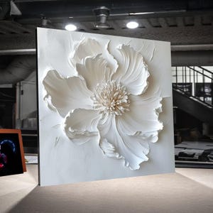 Può includere: Una grande opera d'arte murale floreale tridimensionale bianca. L'opera presenta una peonia strutturata dettagliata con petali a strati e un centro strutturato. L'opera è montata su uno sfondo bianco quadrato, creando un effetto visivo sorprendente.