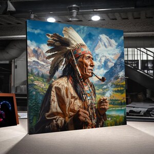May include: A framed canvas print of a Native American man smoking a pipe, set against a backdrop of mountains and a blue sky. The man wears a feathered headdress, beaded necklaces, and a tan-colored shirt. The artwork is displayed in a well-lit room.