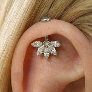 May include: A silver industrial barbell earring featuring a flower design with marquise-cut clear gemstones. The earring is worn in the ear and has a small, flat, silver disc on the top.