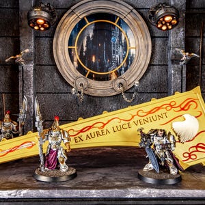 May include: Miniature figurines of armoured warriors with swords and spears are displayed. A large yellow banner with red accents and text is in the centre. The background features a circular window and decorative lighting.