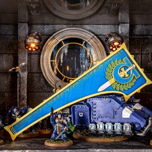 Peut inclure: Diorama d&eacute;taill&eacute; avec des figurines de soldats blind&eacute;s et un char. La sc&egrave;ne comprend une banni&egrave;re bleue avec des bordures et du texte dor&eacute;s, une fen&ecirc;tre circulaire et des &eacute;l&eacute;ments architecturaux. Les couleurs dominantes sont le bleu, l'or et le gris.