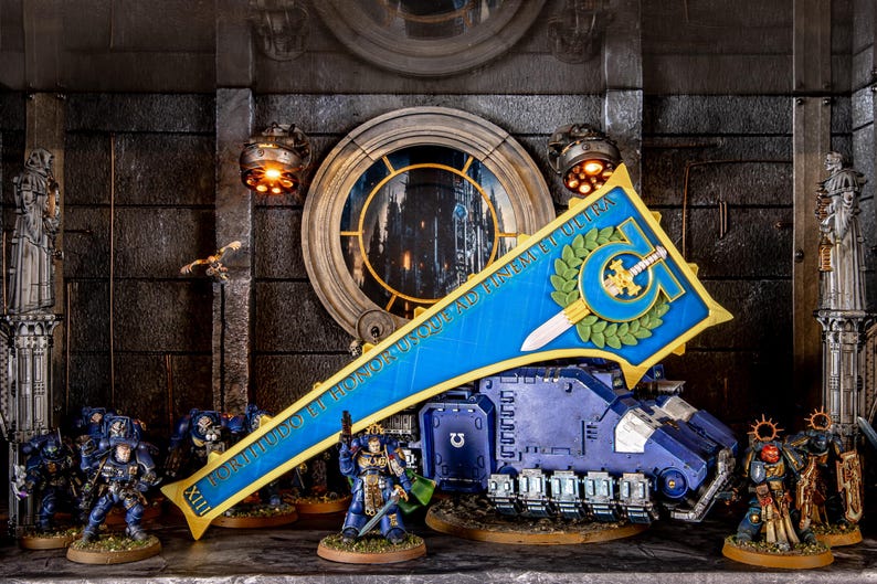Peut inclure: Diorama d&eacute;taill&eacute; avec des figurines de soldats blind&eacute;s et un char. La sc&egrave;ne comprend une banni&egrave;re bleue avec des bordures et du texte dor&eacute;s, une fen&ecirc;tre circulaire et des &eacute;l&eacute;ments architecturaux. Les couleurs dominantes sont le bleu, l'or et le gris.