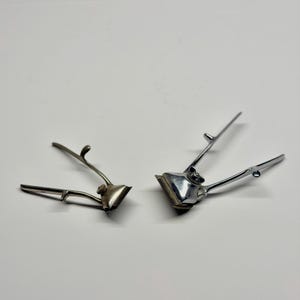 May include: Two vintage manual hair clippers. The clippers are made of silver metal and have a comb-like blade. The handles are curved and have a lever to operate the blades. The clippers are designed for cutting hair.