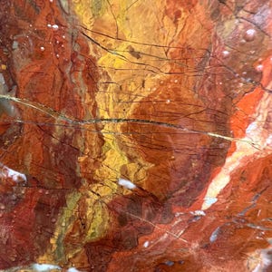 May include: Abstract close-up of a stone surface with a blend of warm colors. The image features a mix of red, orange, and yellow hues, with dark lines and white accents. The texture appears rough and natural, resembling a geological formation.