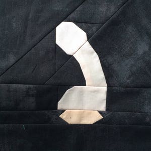 Puede incluir: Una forma de teléfono de tela blanca y beige, hecha de cuadrados de tela patchwork, sobre un fondo negro.