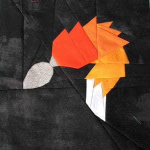 Può includere: Un blocco di trapunta patchwork con un design di volpe stilizzato in tessuto arancione, rosso e bianco su uno sfondo nero.