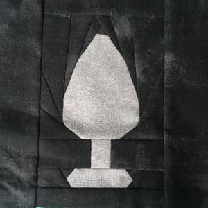 Puede incluir: Una aplicación de tela blanca en forma de árbol estilizado sobre un fondo de tela negro.