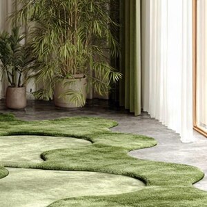 May include: A modern interior scene featuring a light green, organic-shaped rug. Lush green plants in large pots and a green curtain complement the rug. The room has a neutral color palette with natural light.