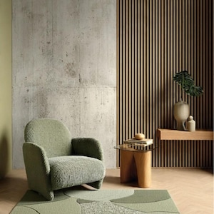 May include: A sage green corduroy armchair with rounded arms and a backrest, positioned on a rectangular area rug featuring a green abstract pattern of overlapping circles and textured sections, set against a concrete and wood slat wall.
