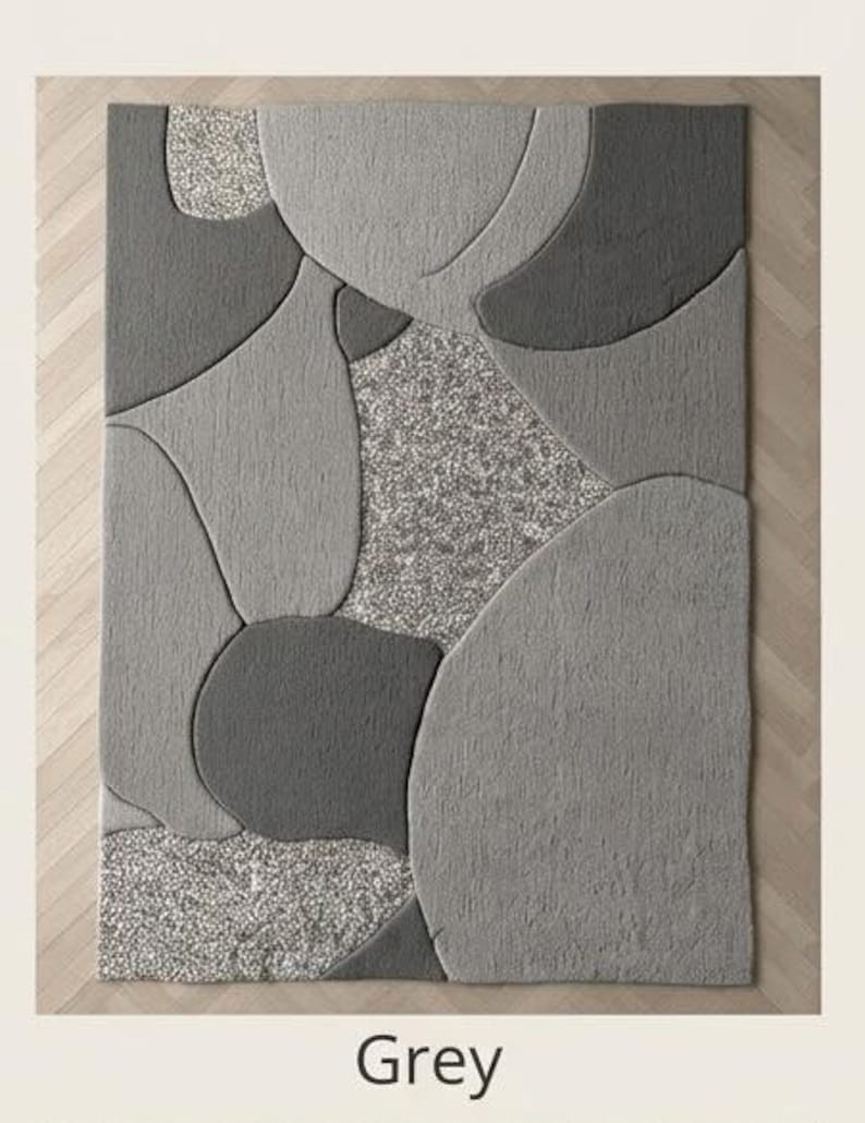 May include: A rectangular area rug with a modern design. The rug features a pattern of overlapping shapes in various shades of gray, with a speckled, lighter gray section in the center. The word "Grey" is printed at the bottom.
