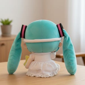 May include: A plush doll with turquoise hair in pigtails, black and pink accents, and a white dress with lace trim. The doll has a yellow star-shaped accessory and a white headband.