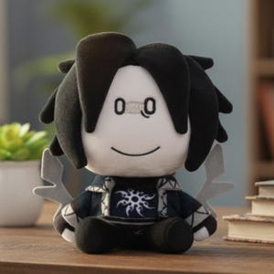 Puede incluir: Un muñeco de peluche con una cara blanca, pelo negro y una expresión sonriente. El muñeco lleva un atuendo azul oscuro y negro con un diseño de sol blanco. Tiene detalles grises en forma de alas y pies negros.