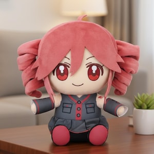 Op de afbeelding: Een pluche pop met een cartoon-achtig ontwerp. De pop heeft roze haar in twee grote zijstaarten, rode ogen en een lachend gezicht. Ze draagt een grijze outfit met rode accenten en roze schoenen. De pop zit op een houten oppervlak.