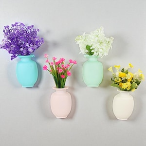 Könnte beinhalten: Vier farbenfrohe Wandvasen, jede mit verschiedenen künstlichen Blumen. Die Vasen sind in den Farbtönen Blau, Mintgrün, Rosa und Weiß gehalten. Die Blumen umfassen lila, weiße, rosa und gelbe Blüten.