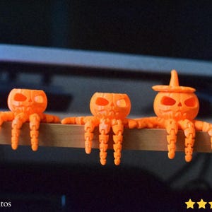 May include: Three orange Halloween octopus figurines. Each has a carved pumpkin head and articulated tentacles. One wears a witch's hat. The figurines are displayed on a wooden surface.