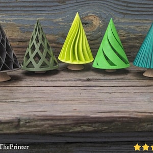 May include: Five decorative cone-shaped trees in varying shades of green and black, each with a unique geometric or spiral design. The trees sit on small, light-colored bases, arranged on a rustic wooden surface. The image includes the text "@JamesThePrinter".