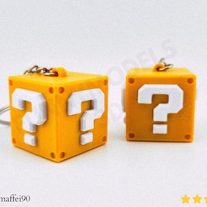 Puede incluir: Dos llaveros amarillos con forma de bloque de interrogación. Cada cubo tiene un signo de interrogación blanco en varias caras. Los llaveros tienen una cadena y un anillo plateados. Los bloques son de color amarillo brillante.
