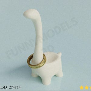 May include: A white dinosaur-shaped ring holder with a gold ring on its neck. The ring holder has a long neck and a small bowl-shaped body. The ring is gold with a textured design. The background is a light blue.