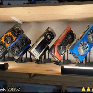 Può includere: Cinque schede grafiche colorate in mostra. Le schede presentano ventole nere e vari schemi di colori, tra cui arancione, blu e rosso. Ogni scheda è montata su un supporto nero, mostrando il loro design e i componenti.