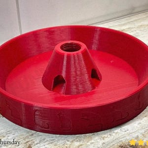 Puede incluir: Un objeto rojo brillante impreso en 3D, con un cono central y una base circular con patrones en relieve. El cono tiene una abertura roscada. El texto "@justinthursday" es visible.