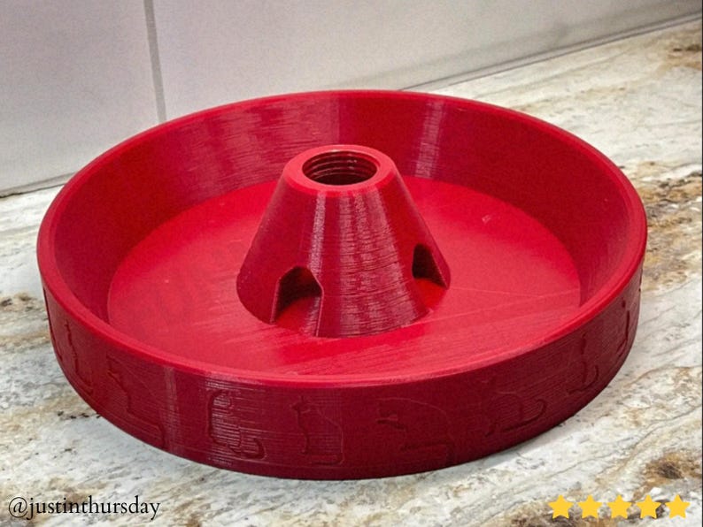 Puede incluir: Un objeto rojo brillante impreso en 3D, con un cono central y una base circular con patrones en relieve. El cono tiene una abertura roscada. El texto "@justinthursday" es visible.
