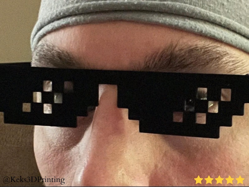 May include: Black pixelated sunglasses with a mosaic design. The sunglasses are worn by a person wearing a gray beanie. The image includes the text "@Keks3DPrinting" and five gold stars.